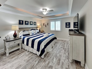 Ein Schlafzimmer mit Bett, Nachttischen, Kommode, Deckenventilator und Wandbildern.