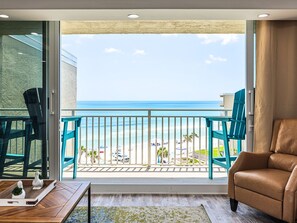Un balcon avec vue sur la plage, un fauteuil en cuir et une table en bois agrémentée d’objets décoratifs.