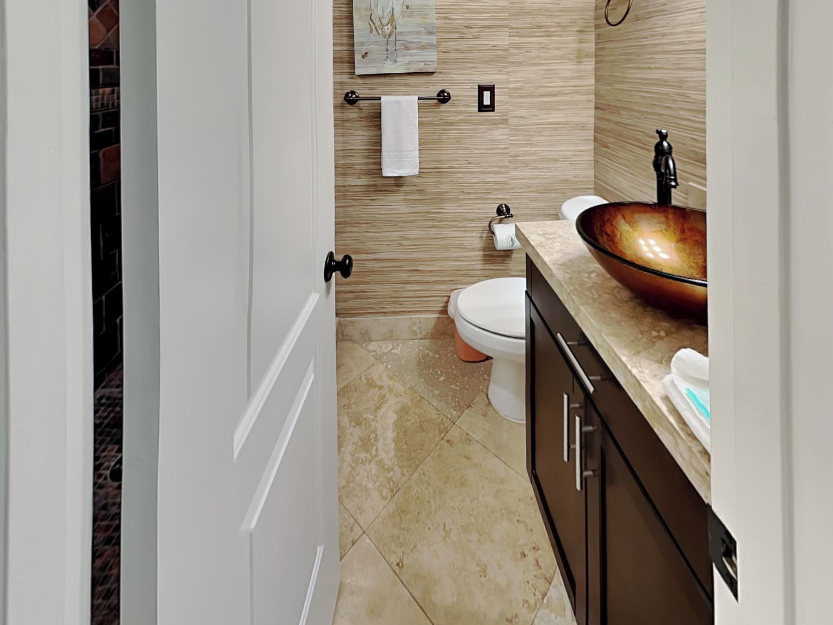 A bathroom with a white toilet, a beige sink with a copper basin, and a towel hanging on a rack.