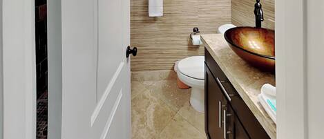 A bathroom with a white toilet, a beige sink with a copper basin, and a towel hanging on a rack.
