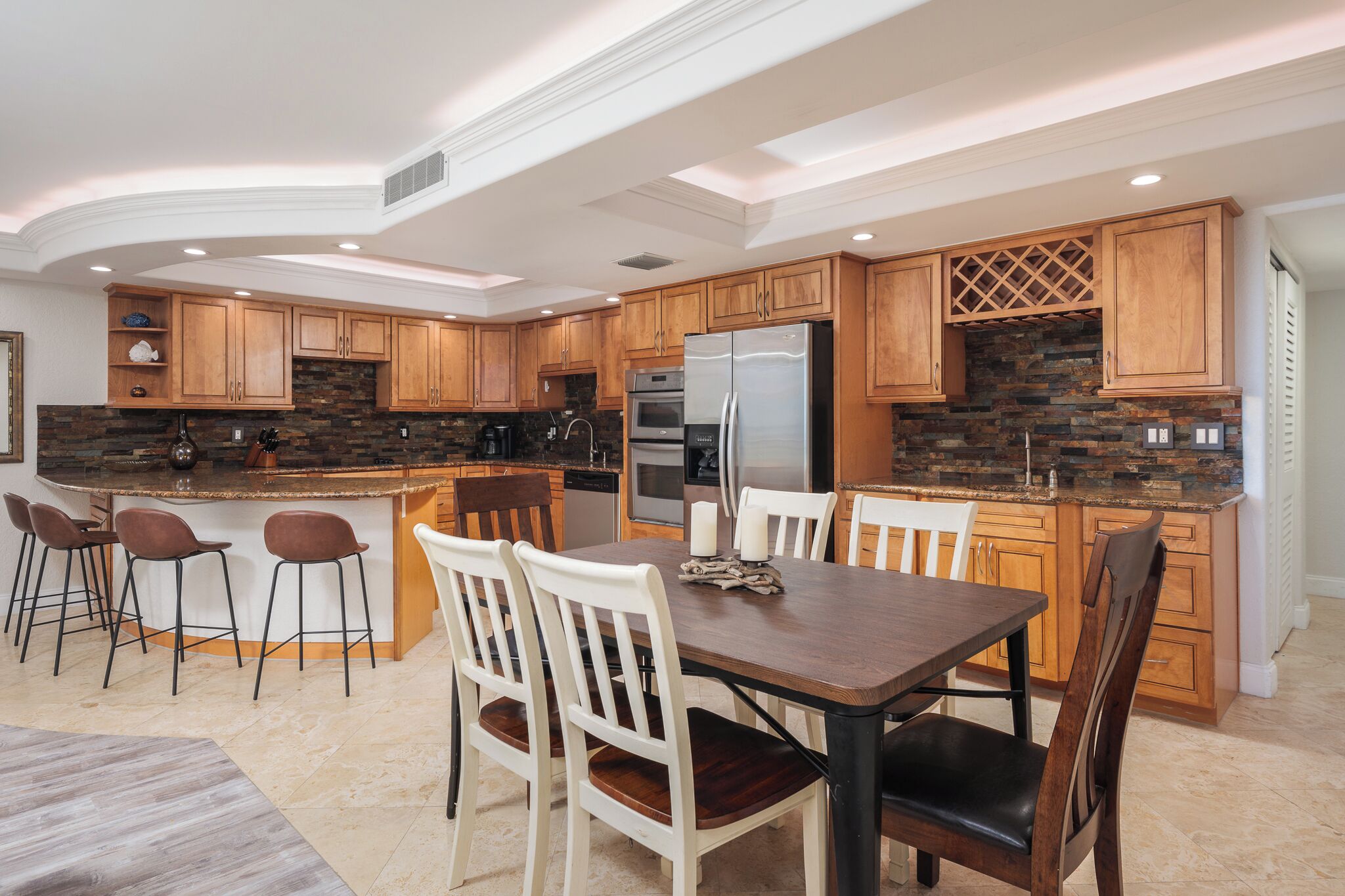 A modern kitchen with wooden cabinets, a central island, bar stools, and a dining table with chairs.