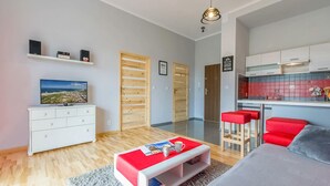 A modern apartment with a TV, wooden doors, a kitchen with red bar stools, and a grey sofa. - Gorgeous apartment in Darlówko with WiFi (Darlówko)