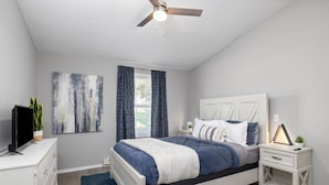 Une chambre à coucher avec un lit, une table de chevet, un téléviseur et un ventilateur de plafond.