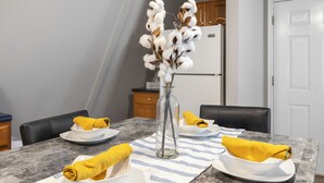 Une table à manger dressée avec des assiettes, des bols et des serviettes jaunes, et un vase rempli de fleurs de coton placé au centre.