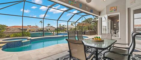 A poolside area with a glass enclosure, outdoor furniture, and a ceiling fan.