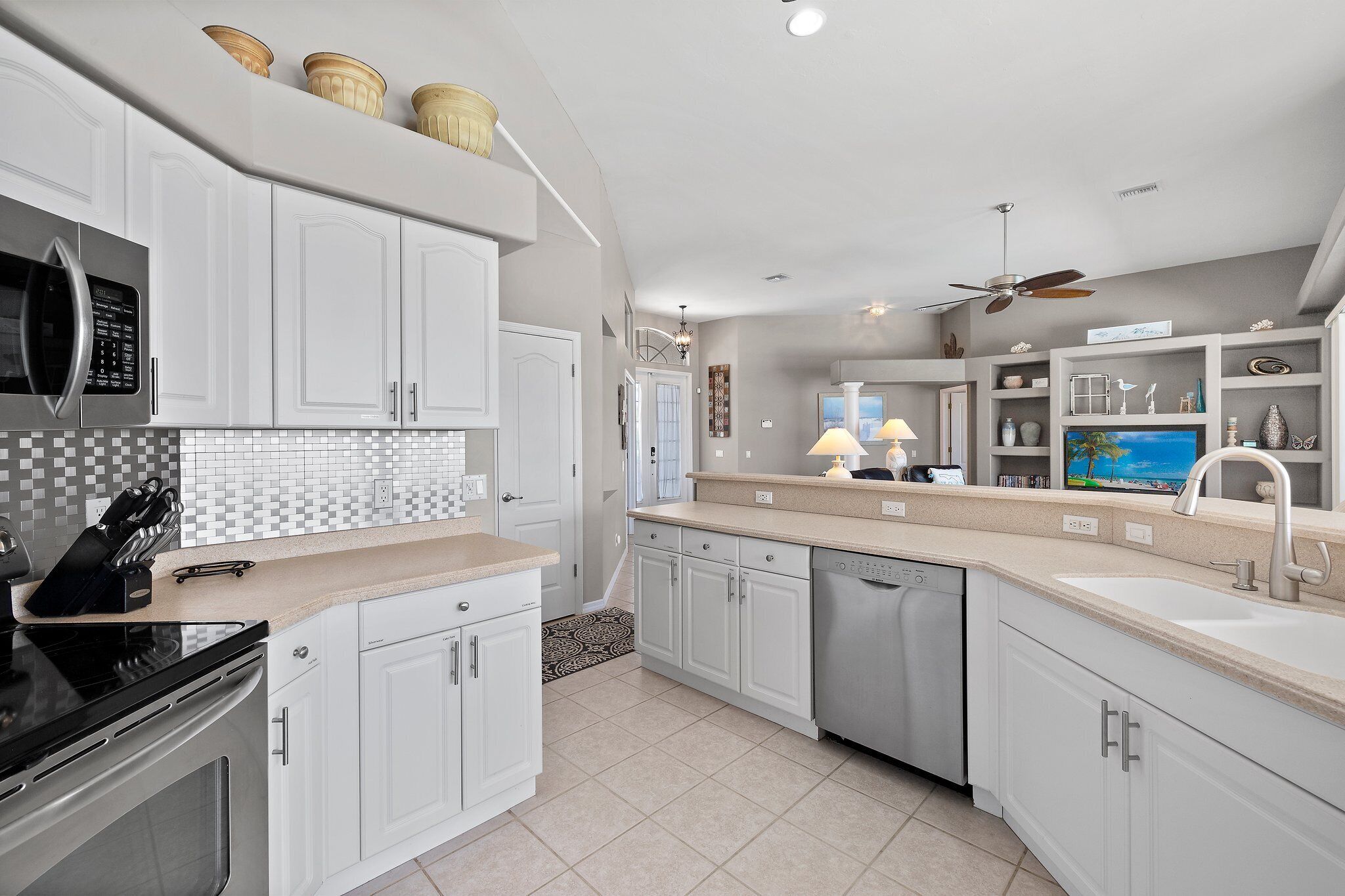 Una cocina moderna con armarios blancos, microondas, lavavajillas y ventilador de techo.