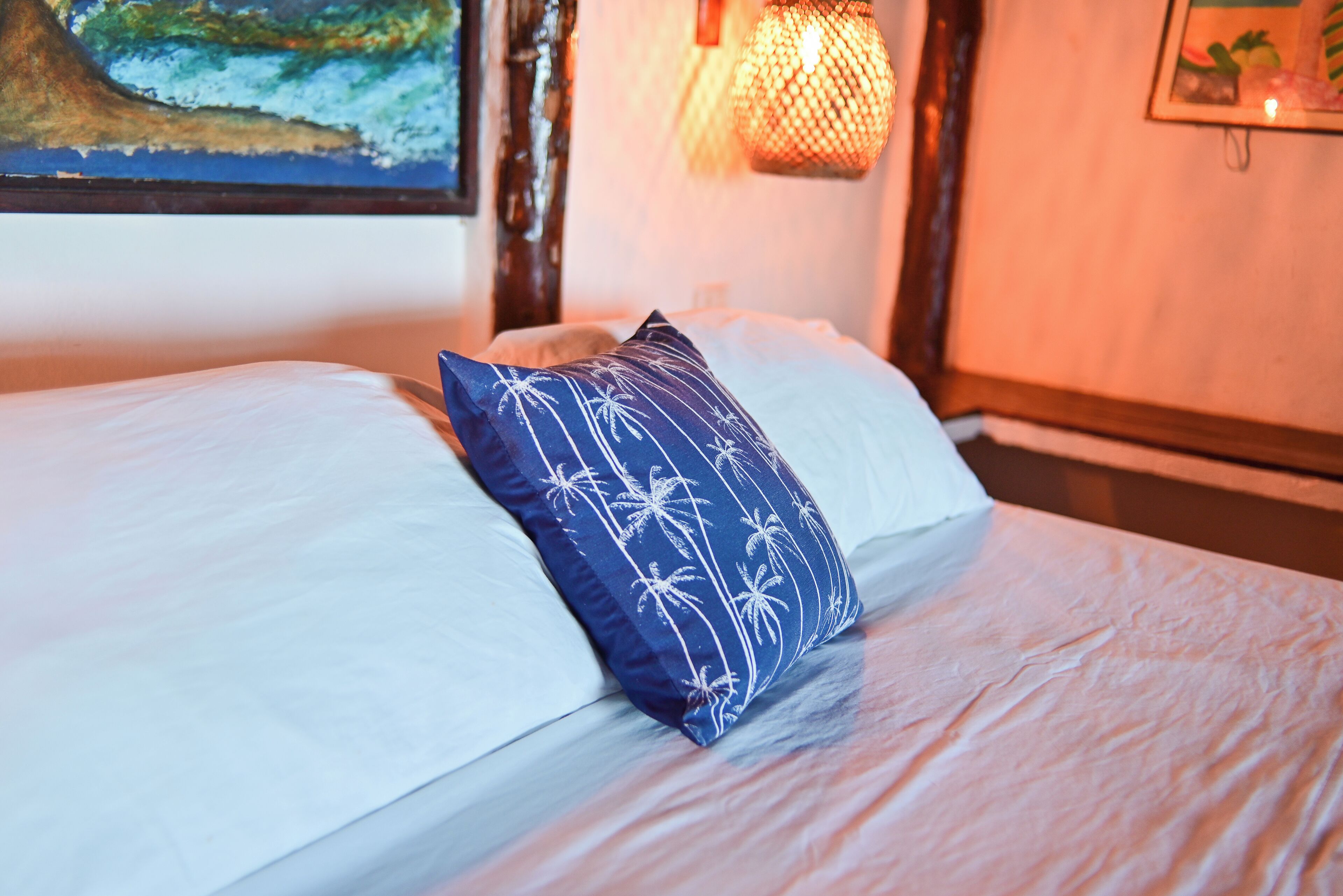 A bed with white linens and a blue pillow with palm tree patterns.