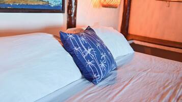 A bed with white linens and a blue pillow with palm tree patterns.