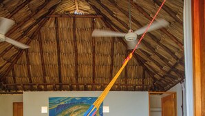 Une pièce avec un lit, un hamac, un ventilateur de plafond et un tableau représentant un poisson au mur.