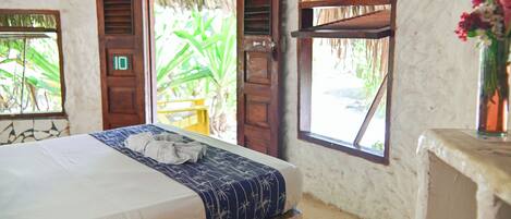Una habitación con cama, una puerta de madera con un número y una ventana con vistas a zonas verdes.