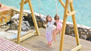 Une balançoire en bois, avec une pancarte indiquant : « C’EST ÇA, LA BELLE VIE », installée au bord de l’eau.