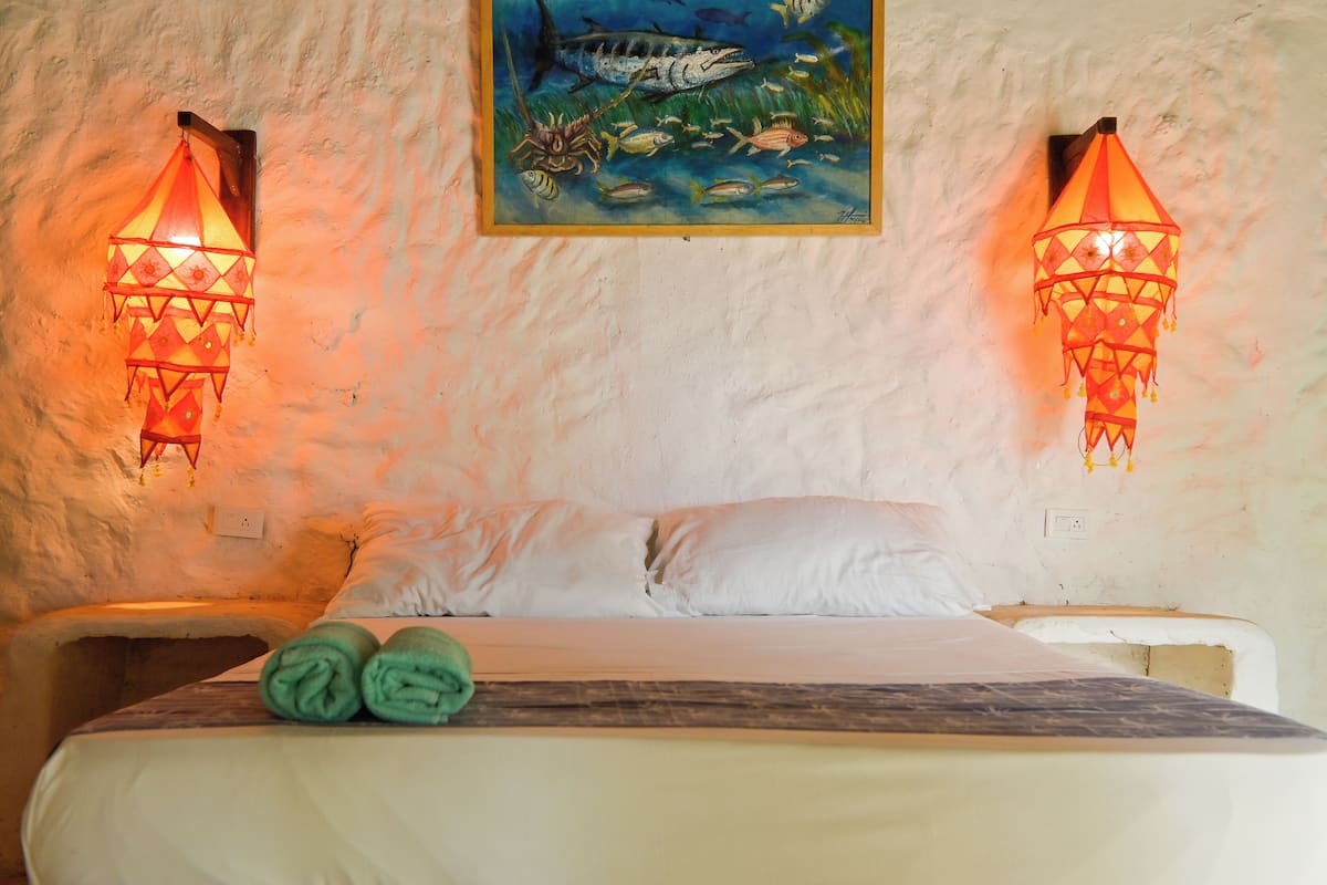 Un lit avec du linge de lit blanc, deux lampes fixées au mur et un tableau représentant la vie marine au-dessus du lit.