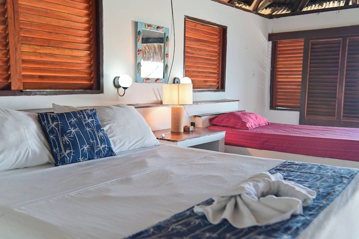 Une chambre d’hôtel avec un lit, une table de chevet avec une lampe, une commode et une fenêtre avec des volets en bois.