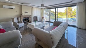 A spacious living room with a fireplace, a large window with a view of a pool, and modern furniture. - Huzur villa  (Izmir)