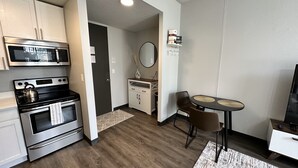 A modern kitchen with stainless steel appliances, a dining area with a round table and chairs, and a small living space with a TV. - Boho Loft / Skyline View / Walk to Arena Events (Des Moines)