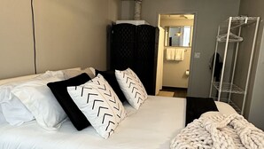 A modern hotel room with a large bed, a hanging light fixture, a wardrobe, and a shower area. - Boho Loft / Skyline View / Walk to Arena Events (Des Moines)