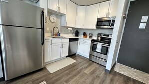 A modern kitchen with stainless steel appliances, white cabinetry, a wooden floor, and a clock on the wall. - Boho Loft / Skyline View / Walk to Arena Events (Des Moines)