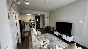A modern living room with a sofa, a coffee table with flowers, a flat-screen TV, and a kitchen in the background. - Boho Loft / Skyline View / Walk to Arena Events (Des Moines)