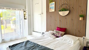 Ein Schlafzimmer mit Bett, Fenster, Tür und einer Wand mit vertikalen Holzleisten und einer hängenden Pflanze.
