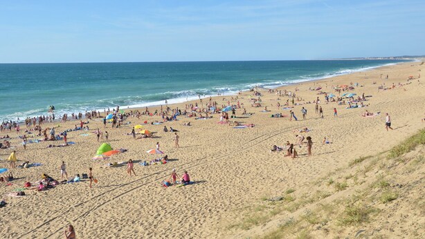 Ein voller Strand mit Menschen, die sonnenbaden und schwimmen.