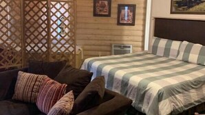 A cozy room with a bed, a couch, and a ceiling fan. There are framed pictures on the wall and a wooden partition.