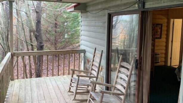 A wooden porch with rocking chairs and a glass door leading inside.
