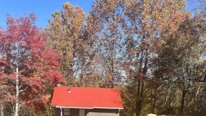 A small, single-story building with a red roof, situated on a gravel driveway surrounded by trees with autumn foliage.