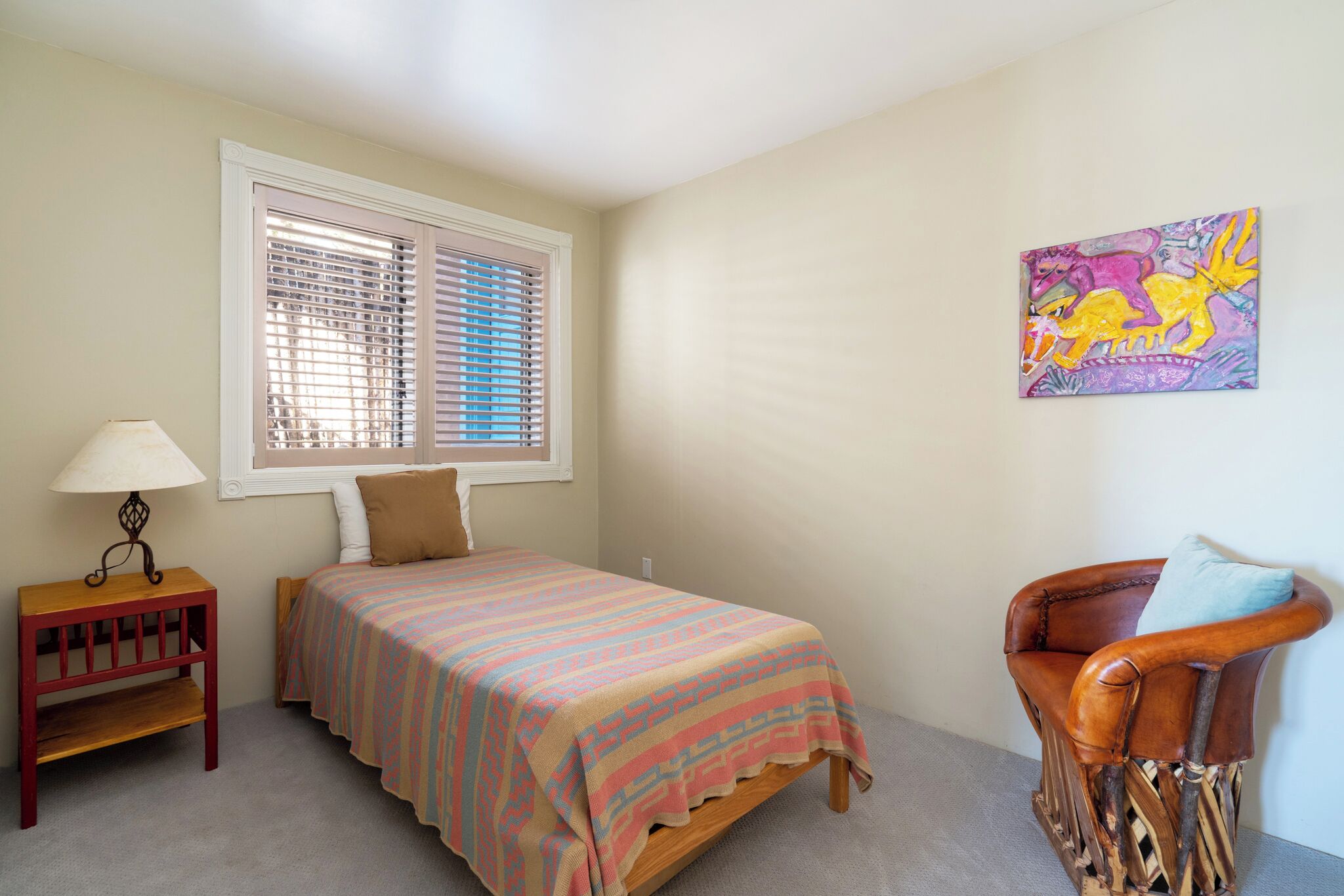A bedroom with a bed, a chair, a nightstand, a window with blinds, and a wall-mounted painting.