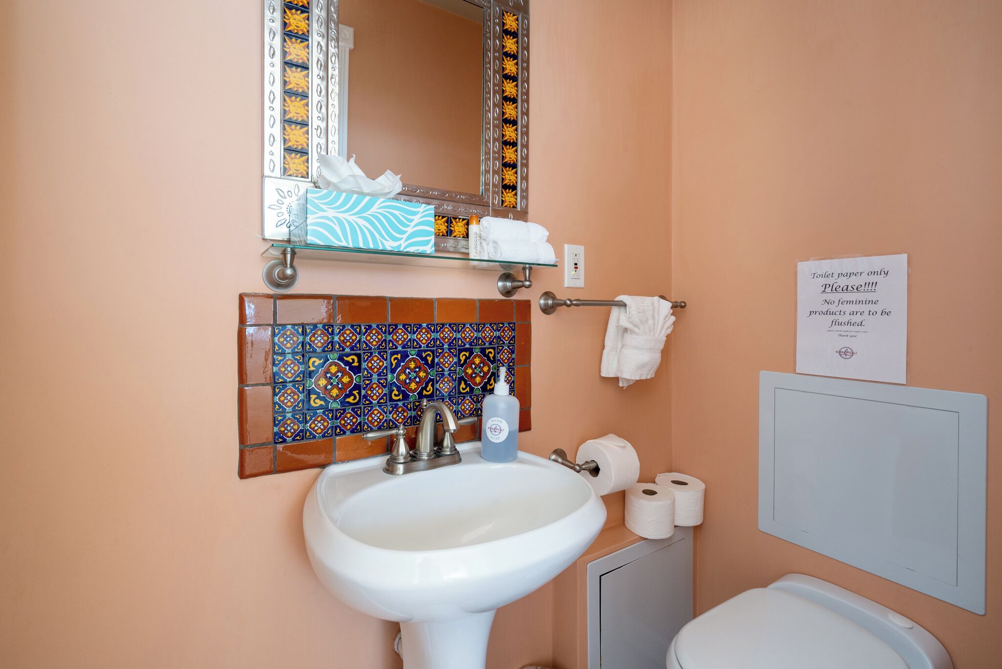 A bathroom with a white sink, a mirror, a toilet, and a sign about toilet paper usage.