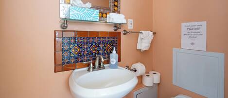 A bathroom with a white sink, a mirror, a toilet, and a sign about toilet paper usage.