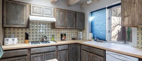 A kitchen with wooden cabinets, a tiled backsplash, a window with blinds, and a dishwasher.