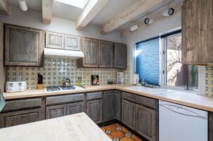 Una cocina con armarios de madera, salpicadero de azulejos, una ventana con persianas y un lavavajillas.