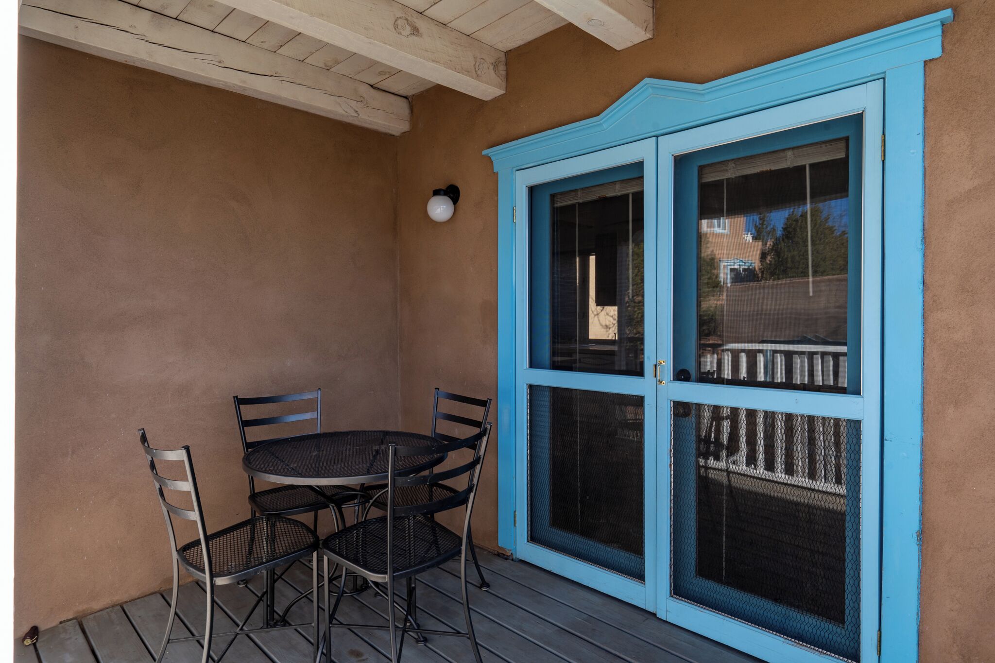 Eine Terrasse mit rundem Tisch und vier Stühlen, einer blauen, rahmenlosen Schiebetür und einer Wandleuchte.