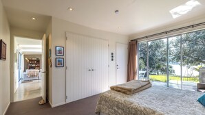 A bedroom with a large bed, a wardrobe, and a sliding glass door leading to a balcony with a view of greenery and a body of water. - Bonnie Doon l Be My Guest Waiheke  (Waiheke Island)