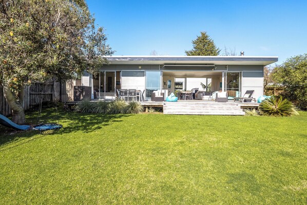 Une maison moderne dotée d’un patio couvert, d’une balançoire et d’une pelouse bien entretenue.