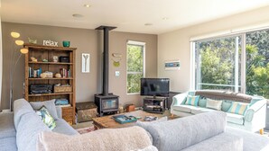 A cozy living room with a fireplace, a television, and comfortable seating. - Bonnie Doon l Be My Guest Waiheke  (Waiheke Island)