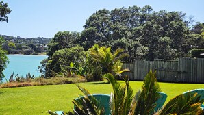 A backyard with a lawn, a wooden fence, and a view of a lake. - Bonnie Doon l Be My Guest Waiheke  (Waiheke Island)