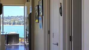 A hallway leading to a balcony with a view of a body of water and hills. - Bonnie Doon l Be My Guest Waiheke  (Waiheke Island)