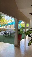 Un espacio al aire libre cubierto con suelo de baldosas, sillas blancas y plantas en macetas.