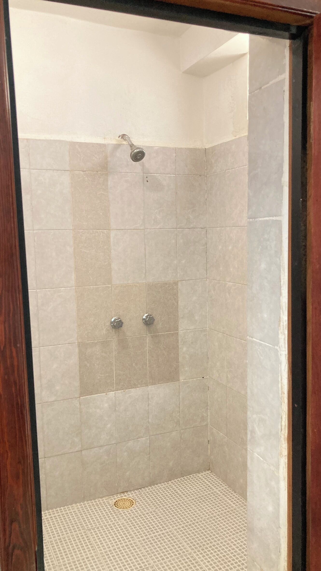Ducha con azulejos color beige y un desagüe en la parte inferior.