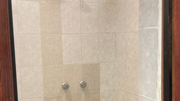Ducha con azulejos color beige y un desagüe en la parte inferior.