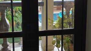 A view through a window with a metal grid, revealing a pool area with a tiled floor and potted plants. - Mansión Serrano  (El Fuerte)