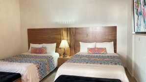 A hotel room with two beds, each with a patterned bedspread and pillows, a wooden headboard, and a nightstand with a lamp. - Mansión Serrano  (El Fuerte)