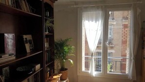 A room with a large window, a bookshelf, and a potted plant. - Cozy apartment in Paris (Paris)