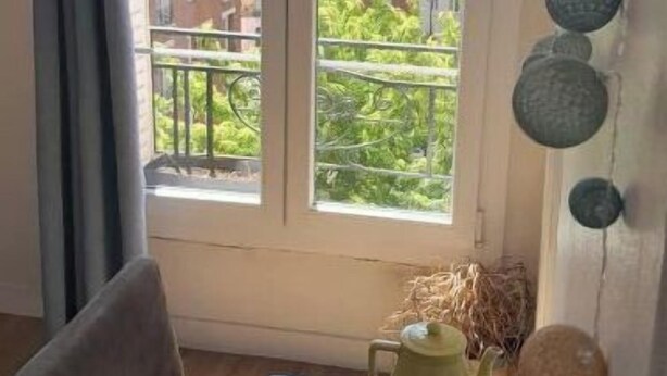 A room with a large window overlooking a cityscape, a wooden table with a yellow teapot, and a chair. - Cozy apartment in Paris (Paris)