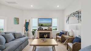 Uma sala de estar com lareira, uma televisão grande e vista para o oceano.