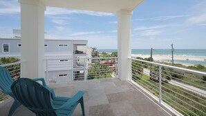 Uma varanda com vista para a praia, piscina e um edifício de fachada branca.