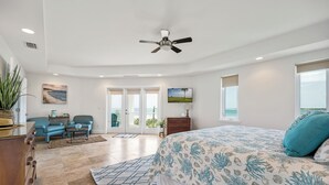 Um quarto espaçoso com uma cama grande, um ventilador de teto e vista para o oceano através das portas de correr de vidro.