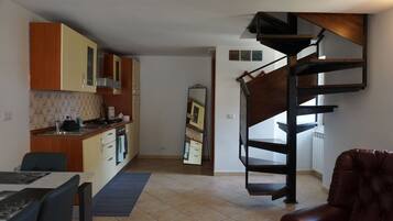 Une cuisine moderne avec des meubles en bois, un coin repas comprenant une table et des chaises, et un escalier en colimaçon menant à un étage supérieur.