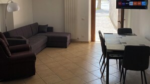 Un salon comprenant un canapé d’angle, une table à manger avec des chaises, un téléviseur à écran plat fixé au mur et un radiateur.